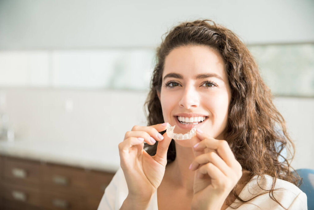 Mulher sorridente segurando alinhador invisível transparente em consulta na Cavasi Odontologia em Juiz de Fora.