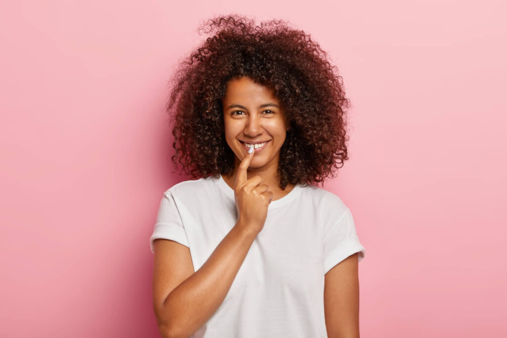 Mulher sorridente com cabelos cacheados aponta para os dentes brancos. Tratamento para dentes manchados na Cavasi Odontologia em Juiz de Fora.