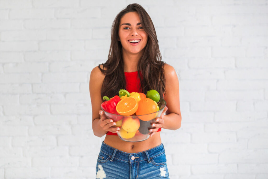 Mulher sorridente segurando tigela com frutas sobre o uso de alinhadores invisíveis em Juiz de Fora na Clínica Cavasi Odontologia.