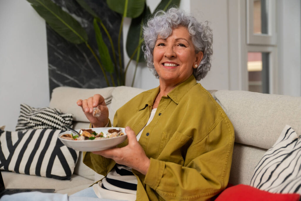 Mulher idosa sorridente comendo de forma saudável. Benefícios da prótese protocolo e implante dentário na Cavasi Odontologia em Juiz de Fora.