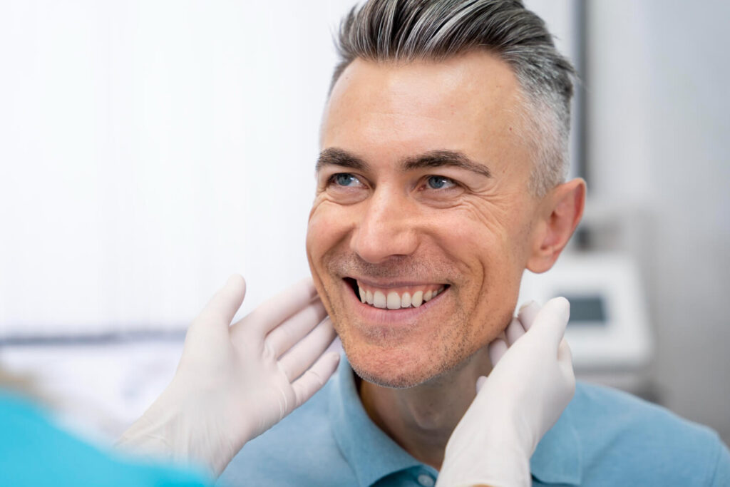 Homem sorridente de cabelos grisalhos recebe avaliação de reabilitação oral na Clínica Cavasi Odontologia em Juiz de Fora.