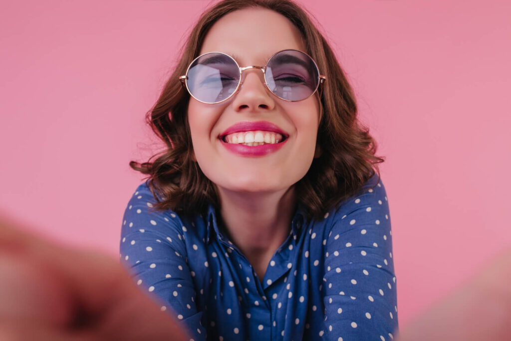 Mulher jovem sorridente de óculos escuros exibindo dentes alinhados por facetas em resina na Cavasi Odontologia em Juiz de Fora MG.