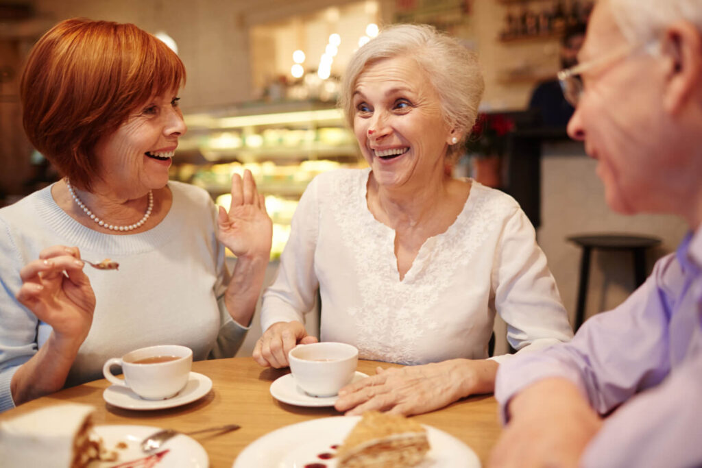Três idosos sorrindo e conversando em um café. Implantes dentários na idade avançada devolvem a qualidade de vida em Juiz de Fora.