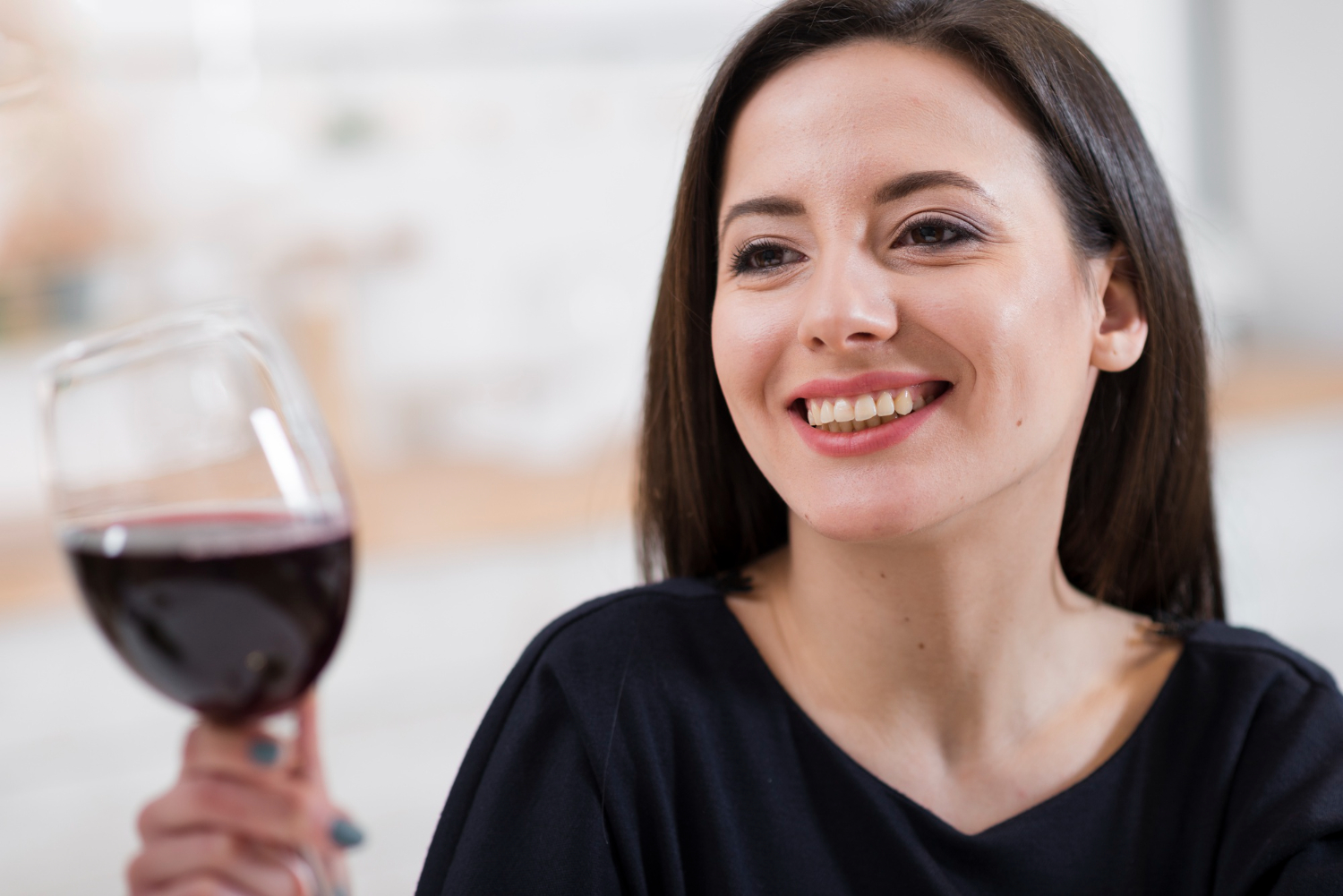 Mulher sorrindo segura taça de vinho tinto. Descubra se as lentes de porcelana mancham com bebidas escuras em clínica em Guarulhos.