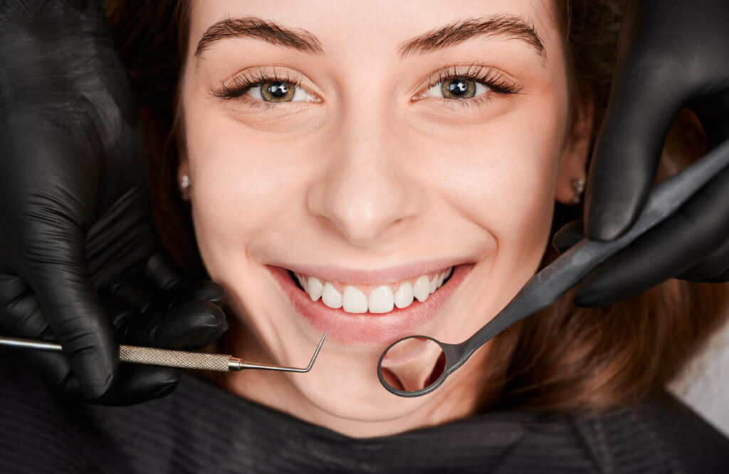 Paciente sorrindo em consulta com instrumentos clínicos. A estética dental em Juiz de Fora permite prever o resultado antes de iniciar.