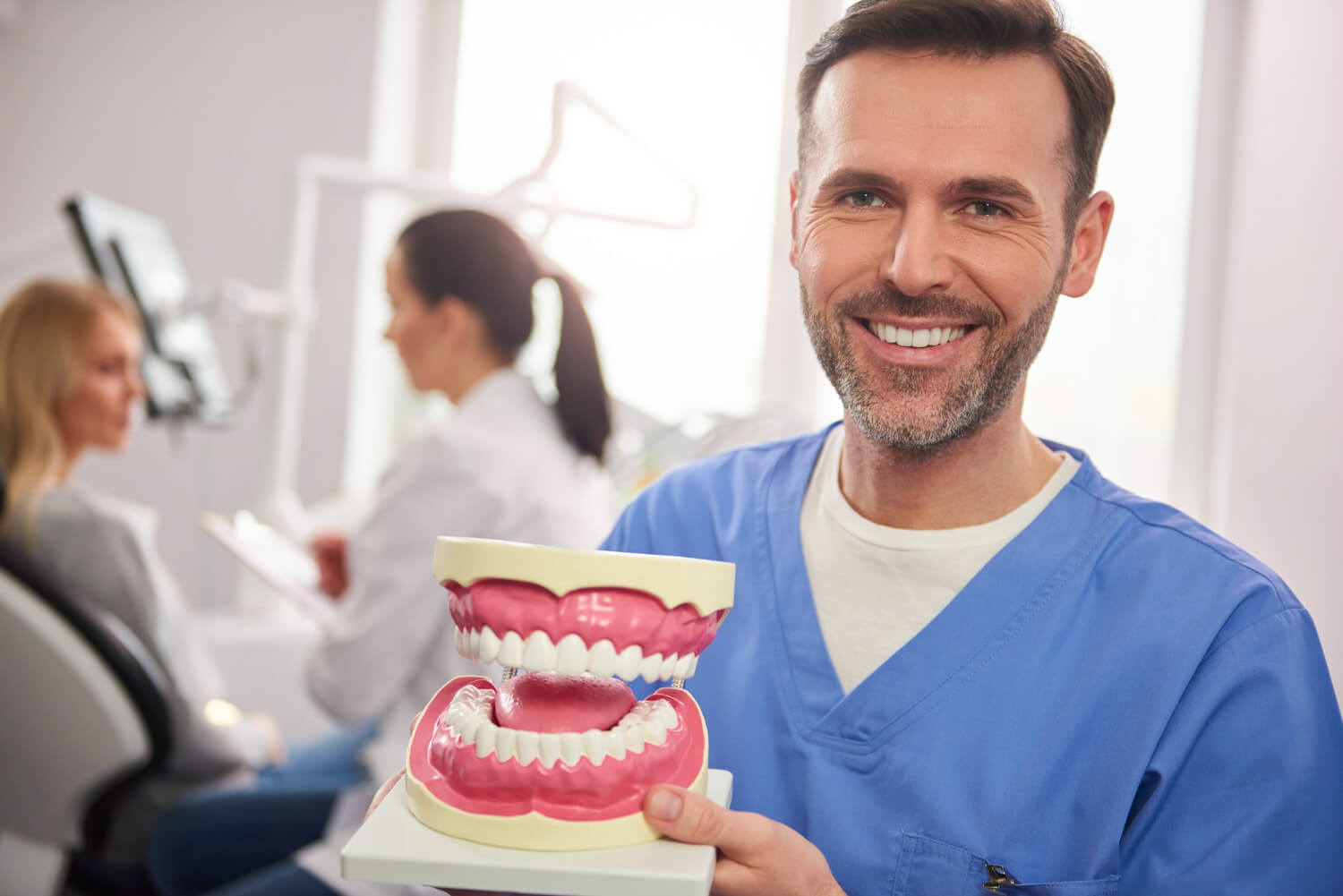 Dentista sorrindo segura modelo de prótese dentária. Entenda as etapas e o tempo do tratamento com prótese protocolo em Juiz de Fora.